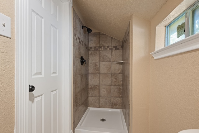 bathroom featuring a tile shower, a textured wall, and a textured ceiling