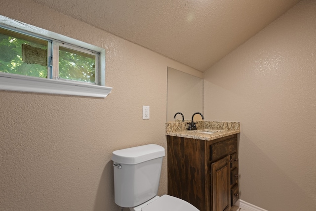 half bath featuring vaulted ceiling, a textured wall, toilet, and vanity