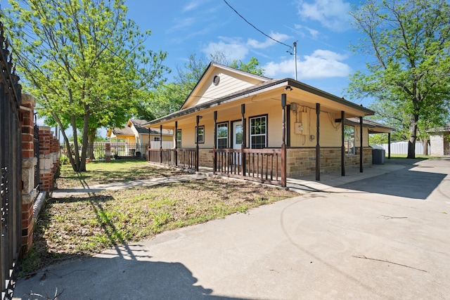 view of front of house with concrete driveway, fence, a porch, and stone siding