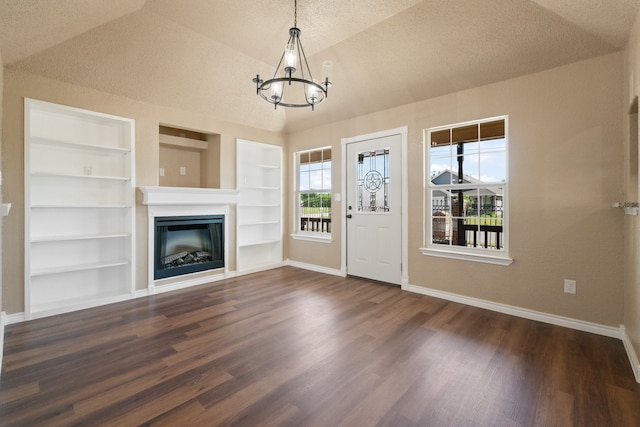 unfurnished living room featuring dark wood finished floors, a glass covered fireplace, baseboards, built in features, and a chandelier