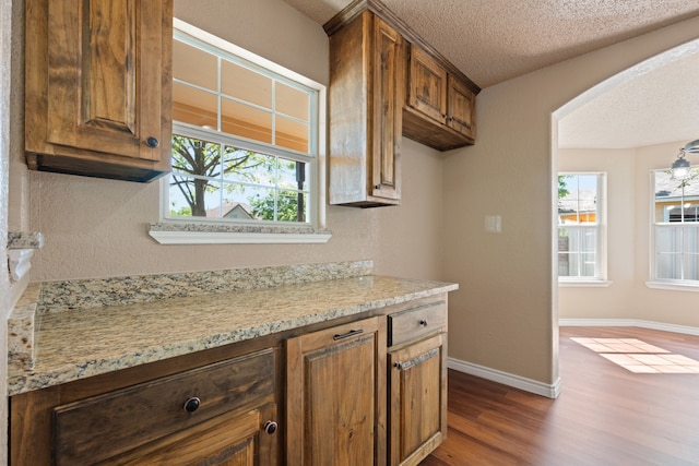 kitchen featuring light stone counters, a textured ceiling, arched walkways, baseboards, and dark wood-style floors
