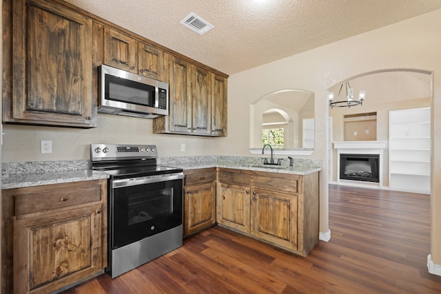 kitchen with a textured ceiling, a sink, brown cabinets, stainless steel appliances, and dark wood-style flooring
