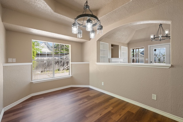 spare room with an inviting chandelier, a textured wall, wood finished floors, and baseboards