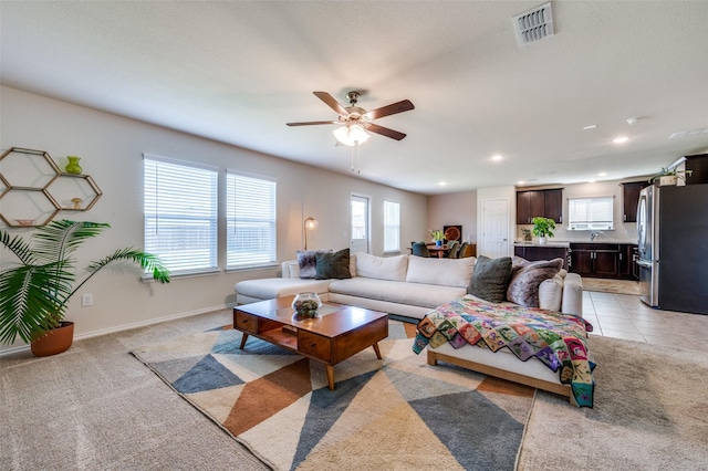 living room featuring light colored carpet, a wealth of natural light, a ceiling fan, and visible vents