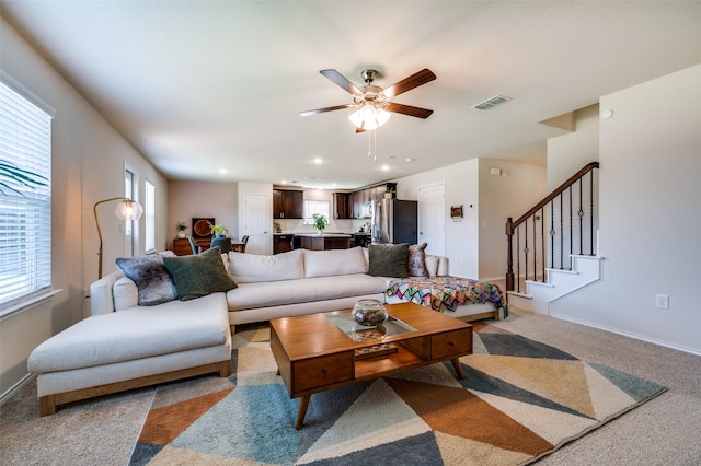 living area with baseboards, a ceiling fan, visible vents, and light colored carpet