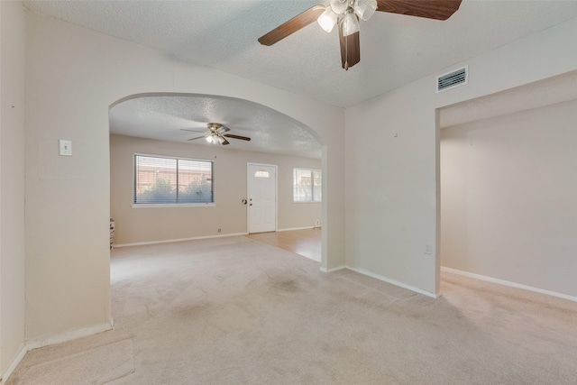 unfurnished room with visible vents, light carpet, arched walkways, a textured ceiling, and ceiling fan