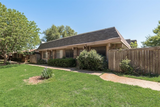 view of front of house with roof with shingles, a front lawn, mansard roof, fence, and brick siding