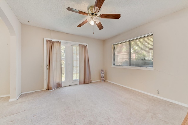 carpeted spare room with arched walkways, a ceiling fan, a textured ceiling, and baseboards