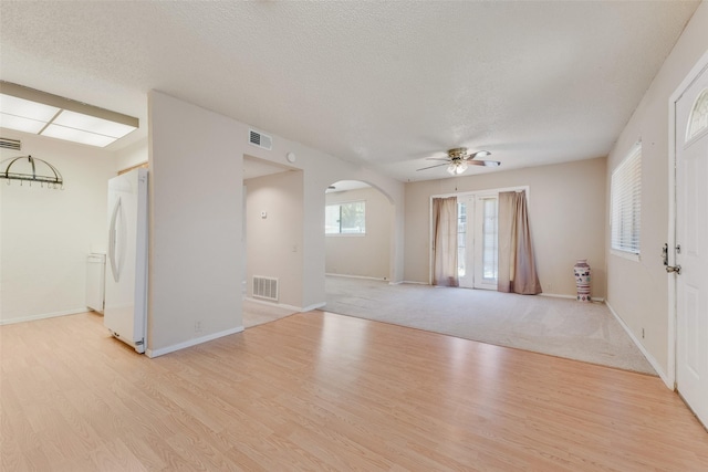 spare room featuring arched walkways, a ceiling fan, visible vents, and light wood-style flooring
