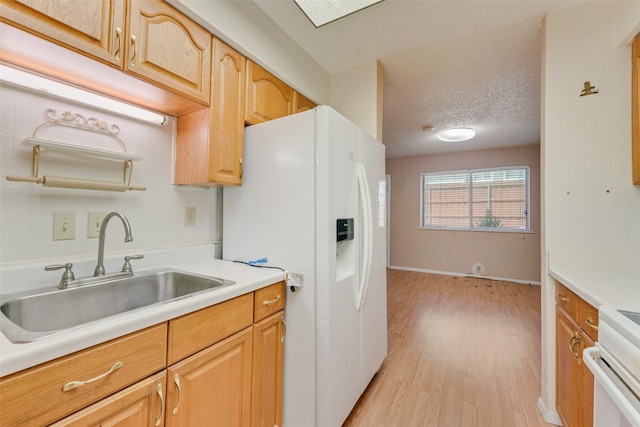 kitchen with a sink, white fridge with ice dispenser, light wood-type flooring, light countertops, and baseboards