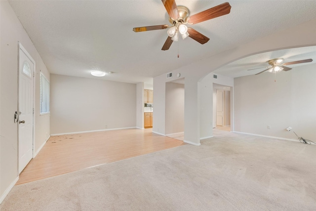 spare room with visible vents, a ceiling fan, arched walkways, baseboards, and light colored carpet