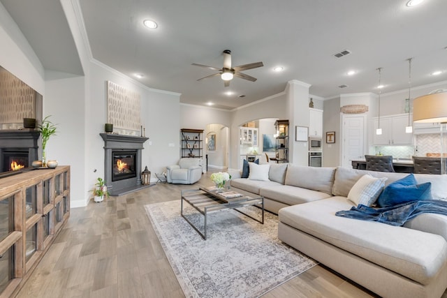 living area featuring ceiling fan, arched walkways, a glass covered fireplace, and light wood-style floors