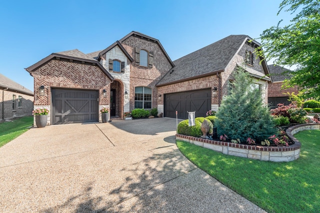 french country inspired facade with driveway, brick siding, an attached garage, a shingled roof, and a front yard