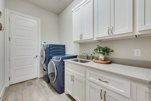 laundry room with light wood-style flooring, a sink, baseboards, separate washer and dryer, and cabinet space