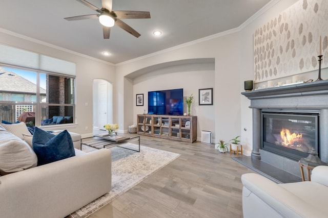 living area featuring wood finished floors, ornamental molding, baseboards, a glass covered fireplace, and ceiling fan