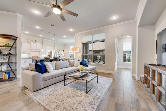 living room with light wood-type flooring, a ceiling fan, arched walkways, and ornamental molding