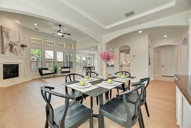 dining room featuring arched walkways, a glass covered fireplace, a ceiling fan, light wood-type flooring, and visible vents