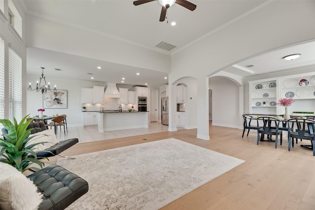 living room featuring crown molding, arched walkways, ceiling fan with notable chandelier, light wood-type flooring, and visible vents