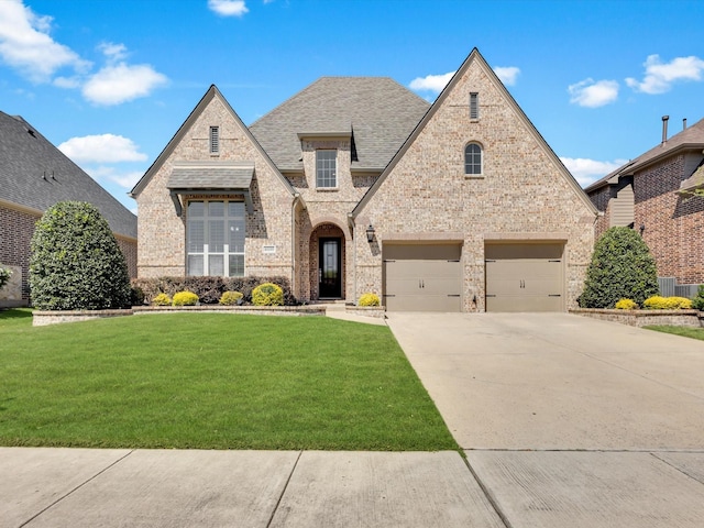 4600 Crossvine Dr, Prosper, TX 75078 - french country style house featuring brick siding, driveway, a front yard, roof with shingles, and an attached garage