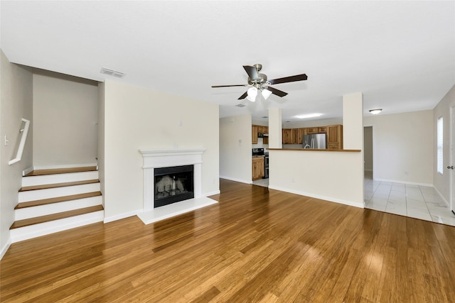12109 Arbor Lake Rd, Rhome, TX 76078 - unfurnished living room with a fireplace with raised hearth, light wood finished floors, visible vents, a ceiling fan, and stairs