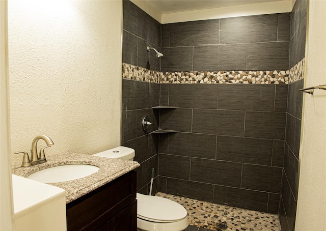 full bathroom featuring toilet, vanity, a textured wall, and a tile shower