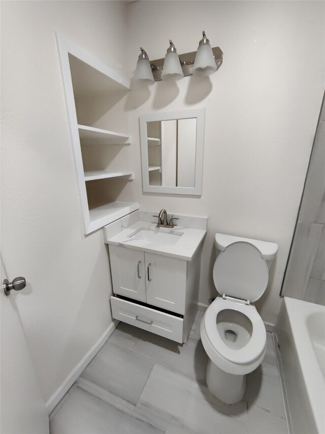bathroom featuring marble finish floor, toilet, vanity, baseboards, and a tub
