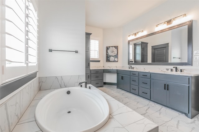 full bathroom featuring marble finish floor, a tub to relax in, double vanity, and a sink