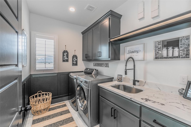 washroom with wainscoting, cabinet space, washing machine and clothes dryer, a sink, and visible vents