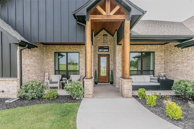 view of exterior entry featuring an outdoor living space, board and batten siding, covered porch, brick siding, and roof with shingles