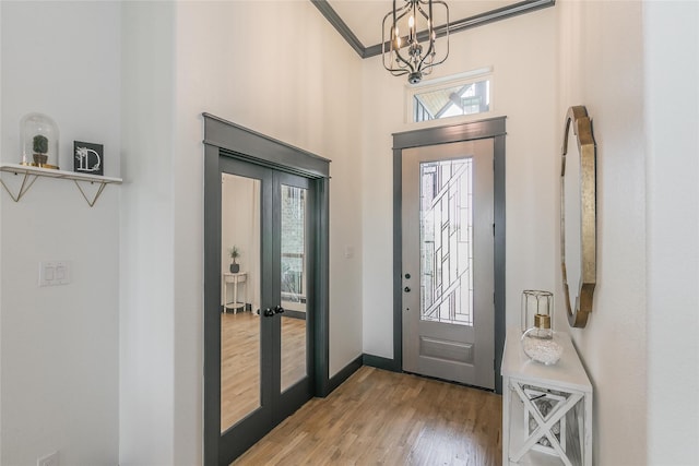 foyer entrance featuring wood finished floors, ornamental molding, baseboards, a notable chandelier, and french doors