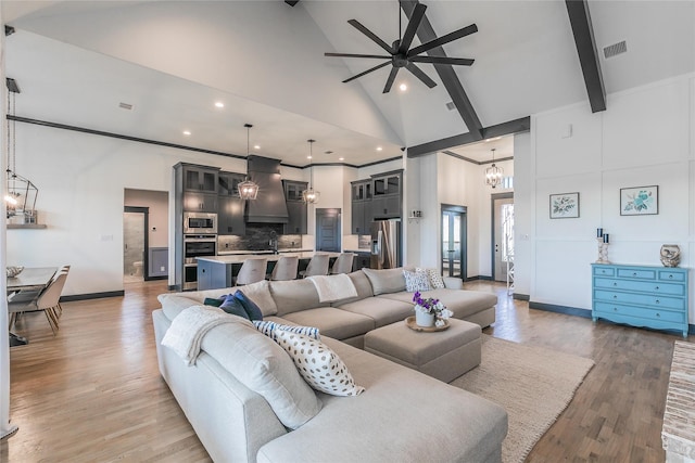 living area with high vaulted ceiling, ceiling fan with notable chandelier, light wood-style flooring, baseboards, and beam ceiling