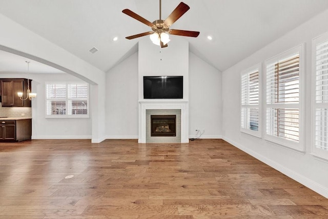 unfurnished living room with a glass covered fireplace, plenty of natural light, visible vents, and ceiling fan with notable chandelier