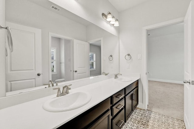full bath with visible vents, a sink, double vanity, and toilet
