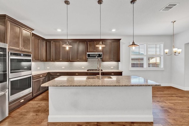 kitchen with light stone countertops, stainless steel appliances, light wood-style flooring, and tasteful backsplash
