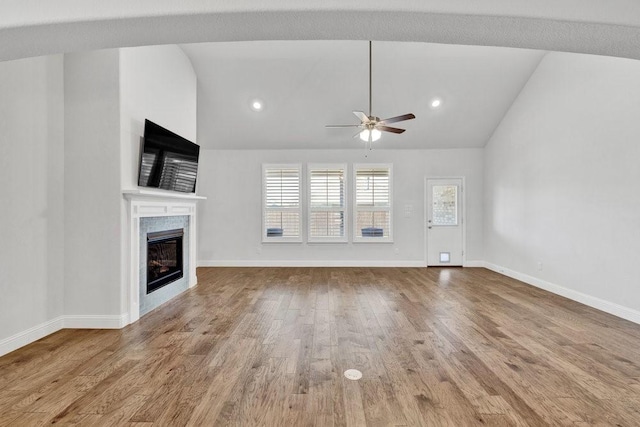 unfurnished living room featuring baseboards, a glass covered fireplace, lofted ceiling, a ceiling fan, and wood finished floors