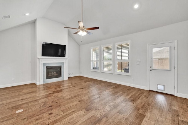 unfurnished living room featuring vaulted ceiling, wood finished floors, a glass covered fireplace, ceiling fan, and visible vents