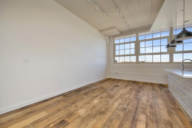 interior space with baseboards, a sink, rail lighting, and wood-type flooring