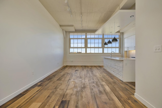 unfurnished room featuring track lighting, hardwood / wood-style flooring, a sink, and baseboards