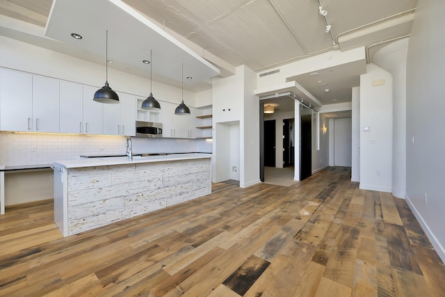 kitchen featuring stainless steel microwave, white cabinetry, open shelves, and light wood finished floors