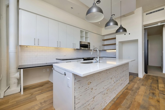 kitchen featuring tasteful backsplash, open shelves, a sink, stainless steel microwave, and visible vents