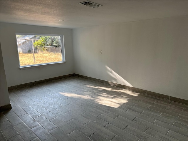 empty room featuring baseboards, visible vents, wood finish floors, and a textured ceiling