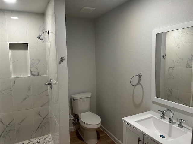 full bathroom with wood finished floors, vanity, a tile shower, toilet, and visible vents