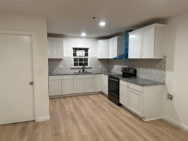 kitchen featuring light wood finished floors, wall chimney range hood, a sink, electric range oven, and white cabinetry