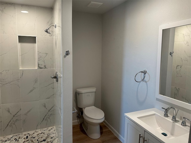 bathroom with wood finished floors, vanity, a tile shower, toilet, and visible vents
