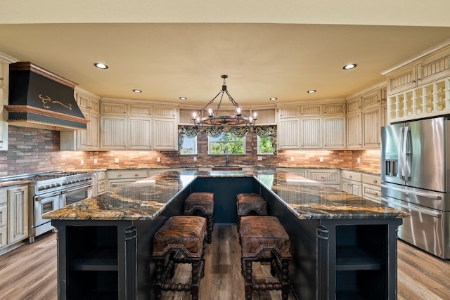 kitchen featuring a kitchen island, cream cabinets, appliances with stainless steel finishes, custom exhaust hood, and a notable chandelier