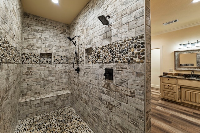 full bathroom featuring tiled shower, visible vents, wood finished floors, crown molding, and vanity