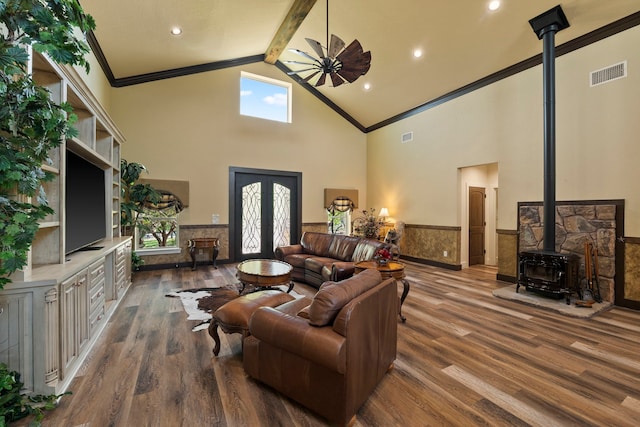 living area featuring wood finished floors, a wainscoted wall, a wood stove, ornamental molding, and visible vents