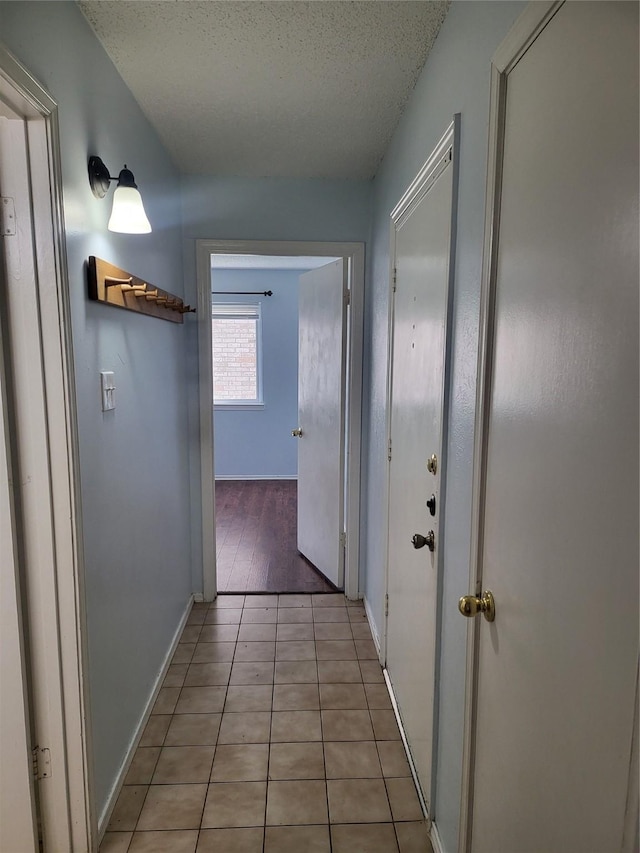 corridor with a textured ceiling, baseboards, and light tile patterned floors