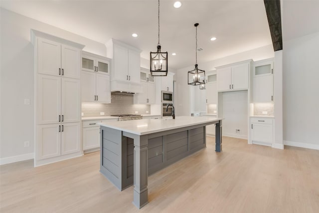 kitchen with decorative backsplash, white cabinetry, stainless steel appliances, and a center island with sink