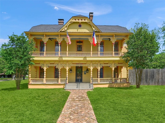 victorian-style house featuring a front lawn, fence, a balcony, and covered porch